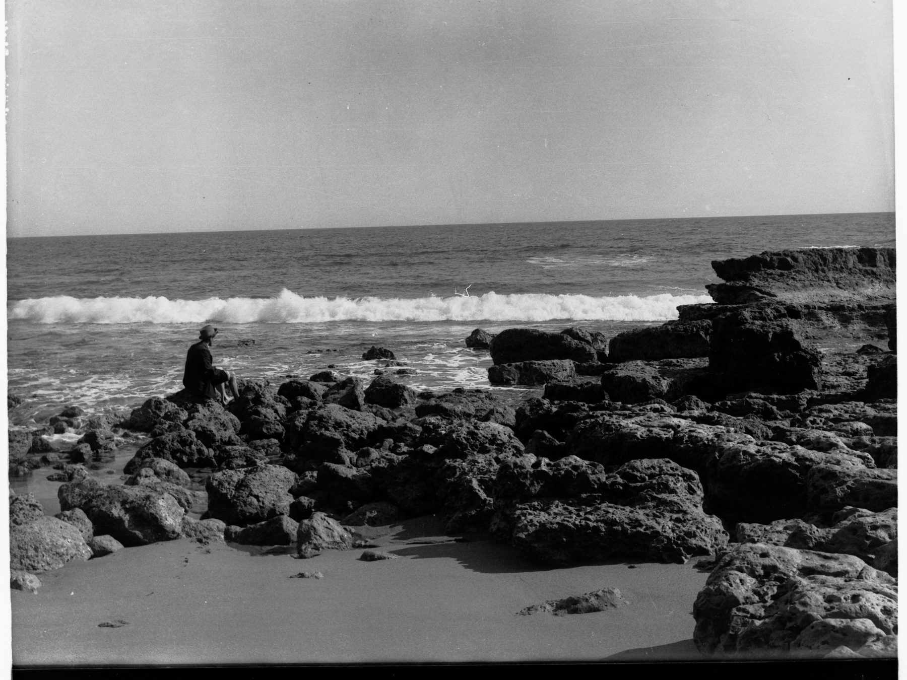 A man sitting alone on the rocks at Port Noarlunga, looking out to sea